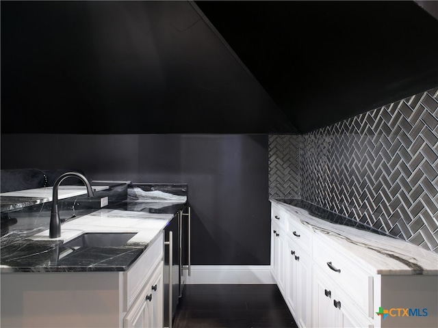 kitchen featuring a sink, light stone countertops, backsplash, and dark wood-type flooring