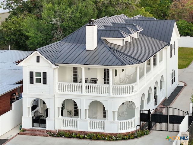 view of front facade with covered porch, a balcony, a standing seam roof, and a gate