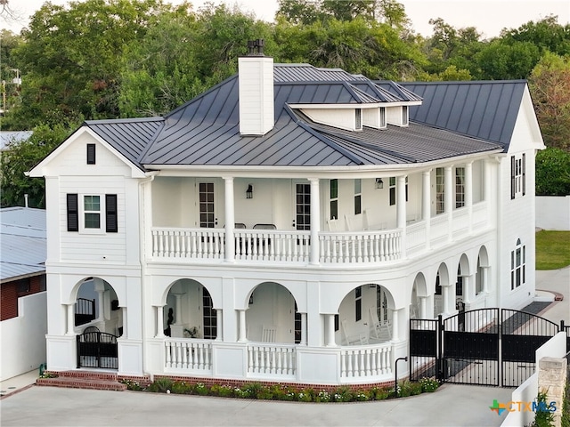 modern inspired farmhouse with a standing seam roof, a gate, a porch, metal roof, and a chimney