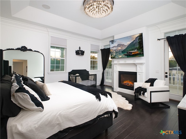 bedroom with dark wood-type flooring, a warm lit fireplace, a tray ceiling, and ornamental molding