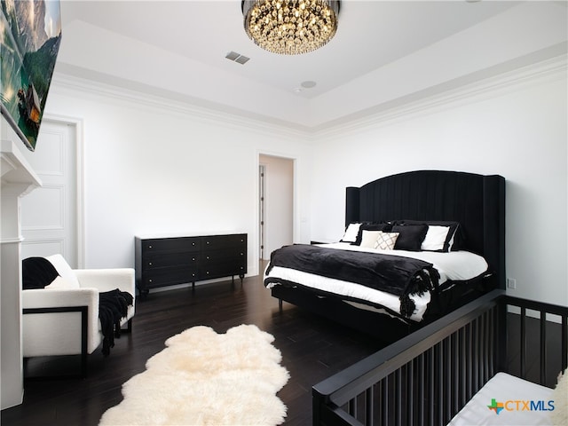 bedroom with visible vents, crown molding, a raised ceiling, and wood finished floors