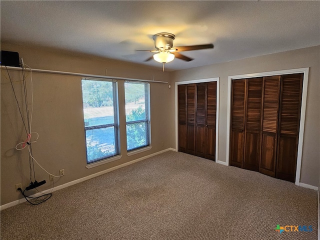 unfurnished bedroom with ceiling fan, two closets, and carpet floors