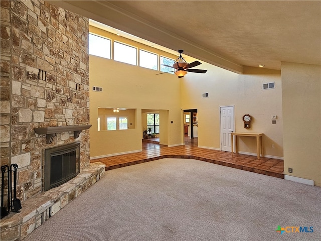 unfurnished living room featuring a towering ceiling, carpet, beamed ceiling, ceiling fan, and a fireplace