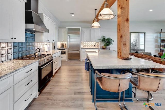 kitchen featuring sink, wall chimney exhaust hood, hanging light fixtures, a breakfast bar, and high end appliances