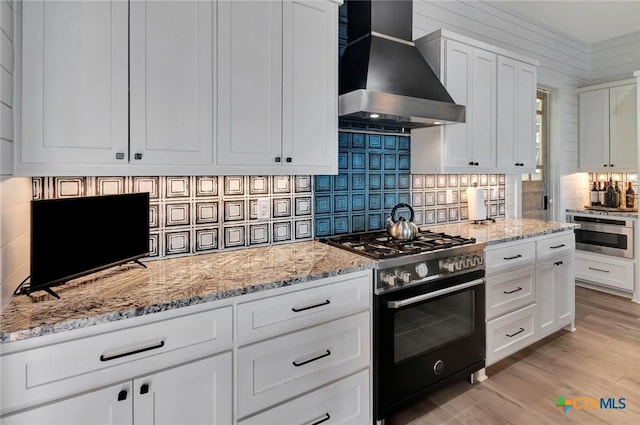 kitchen featuring tasteful backsplash, wall chimney exhaust hood, white cabinets, oven, and range with gas stovetop