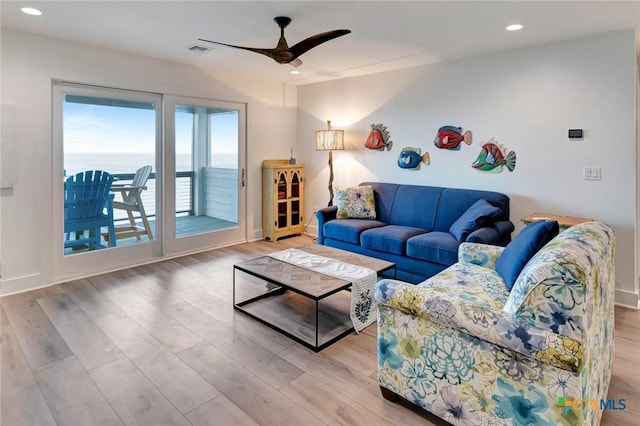 living room with ceiling fan, a water view, and light wood-type flooring