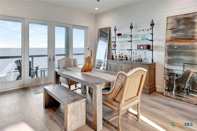 dining space featuring a water view, light hardwood / wood-style flooring, plenty of natural light, and wooden walls