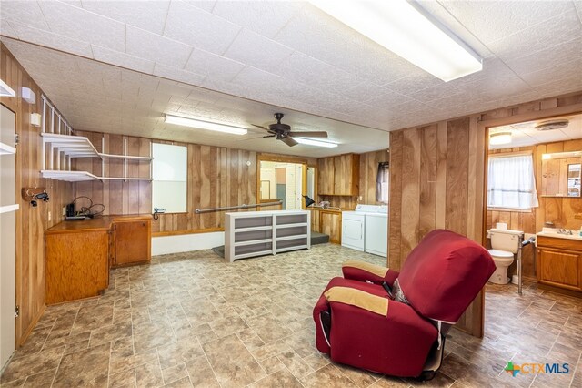 sitting room with wood walls, washing machine and dryer, and ceiling fan