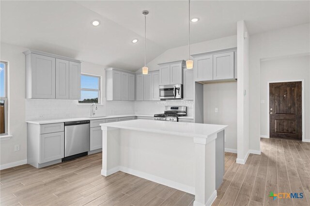 kitchen with sink, a center island, hanging light fixtures, lofted ceiling, and appliances with stainless steel finishes