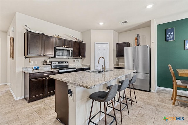 kitchen featuring a sink, light tile patterned flooring, dark brown cabinets, appliances with stainless steel finishes, and a breakfast bar area