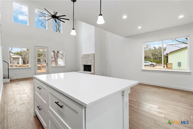 kitchen featuring a stone fireplace, white cabinetry, hanging light fixtures, a kitchen island, and ceiling fan