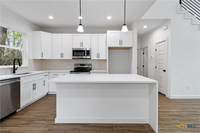 kitchen featuring white cabinetry, appliances with stainless steel finishes, decorative light fixtures, and a kitchen island