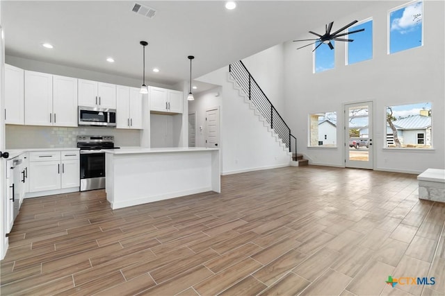 kitchen with stainless steel appliances, decorative light fixtures, a kitchen island, and white cabinets