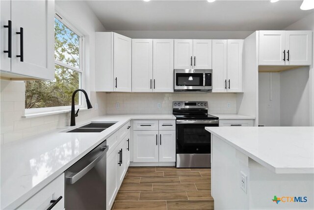 kitchen with sink, appliances with stainless steel finishes, light stone countertops, white cabinets, and decorative backsplash