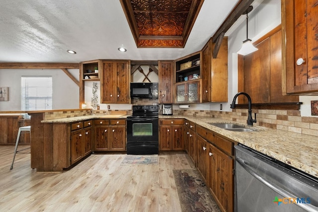 kitchen featuring black appliances, hanging light fixtures, a kitchen breakfast bar, kitchen peninsula, and light hardwood / wood-style flooring