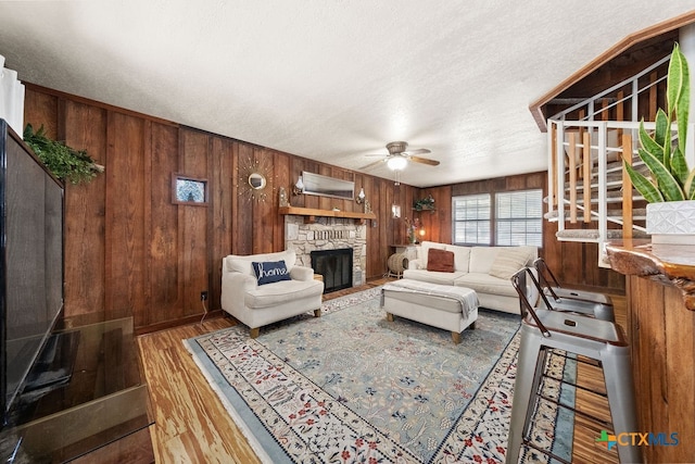 living room with wood-type flooring, a fireplace, a textured ceiling, wooden walls, and ceiling fan