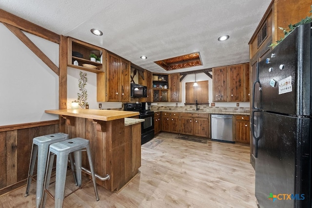 kitchen with black appliances, sink, a kitchen breakfast bar, light hardwood / wood-style floors, and kitchen peninsula