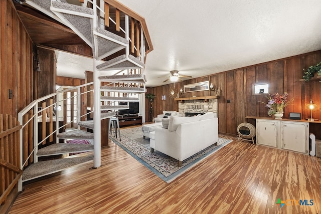 living room with wood walls, a stone fireplace, a textured ceiling, and hardwood / wood-style floors