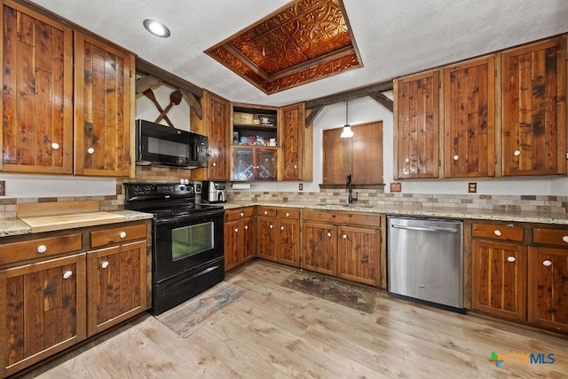 kitchen with hanging light fixtures, black appliances, sink, light stone countertops, and light hardwood / wood-style flooring