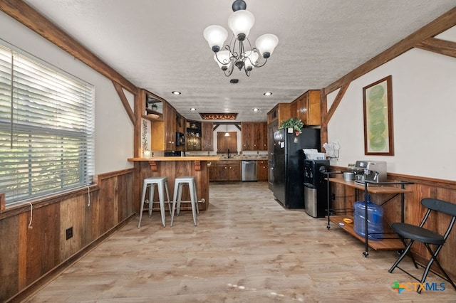 kitchen with kitchen peninsula, a breakfast bar area, stainless steel dishwasher, black refrigerator, and light wood-type flooring