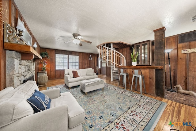 living room with wooden walls, hardwood / wood-style floors, ceiling fan, and a textured ceiling