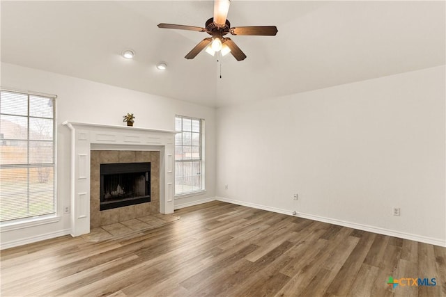 unfurnished living room featuring ceiling fan, a fireplace, hardwood / wood-style floors, and plenty of natural light