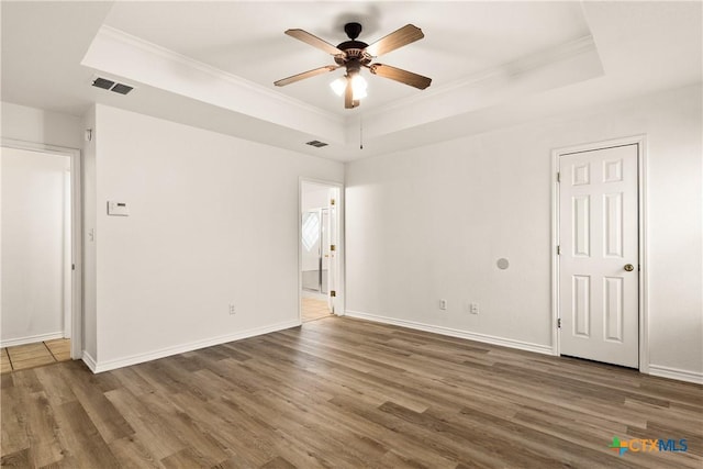 empty room featuring a raised ceiling, crown molding, ceiling fan, and dark wood-type flooring