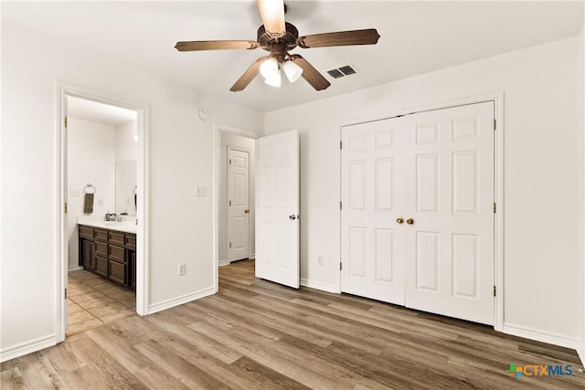 unfurnished bedroom featuring connected bathroom, ceiling fan, sink, light hardwood / wood-style flooring, and a closet