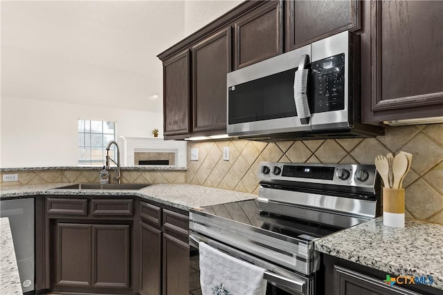 kitchen with light stone countertops, appliances with stainless steel finishes, decorative backsplash, dark brown cabinetry, and sink