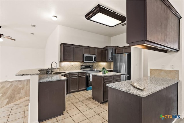 kitchen with sink, light tile patterned floors, a kitchen island, kitchen peninsula, and stainless steel appliances