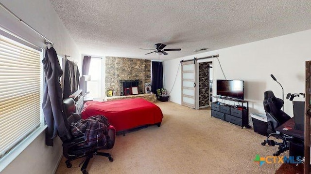 carpeted bedroom featuring ceiling fan, a fireplace, a barn door, and a textured ceiling