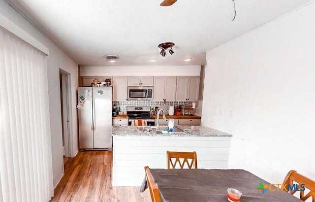 kitchen with backsplash, light stone counters, stainless steel appliances, sink, and light hardwood / wood-style flooring