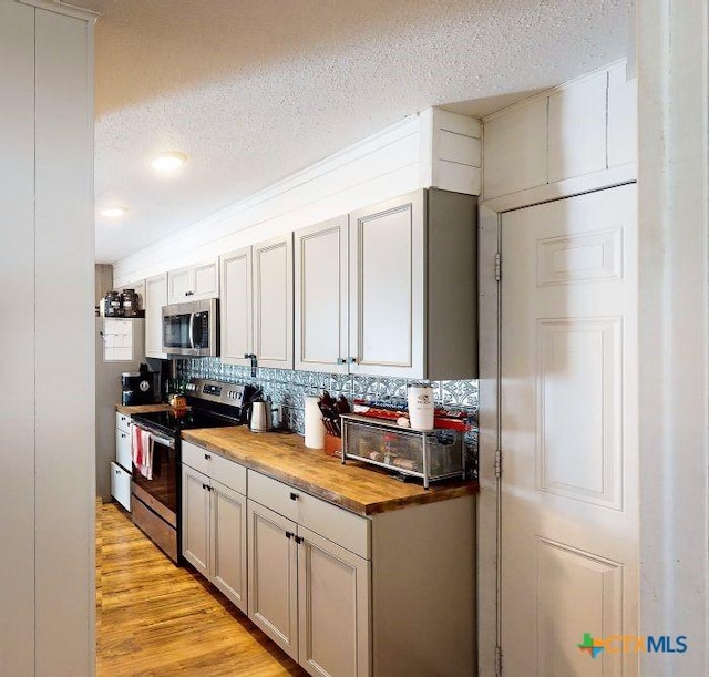 kitchen featuring appliances with stainless steel finishes, tasteful backsplash, a textured ceiling, light hardwood / wood-style floors, and butcher block counters