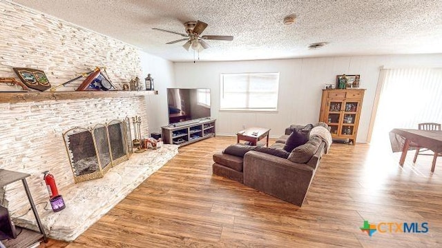 living room with a fireplace, hardwood / wood-style floors, a textured ceiling, and ceiling fan