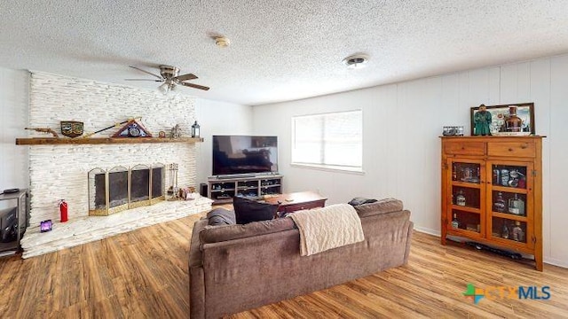 living room featuring a fireplace, a textured ceiling, light hardwood / wood-style flooring, and ceiling fan