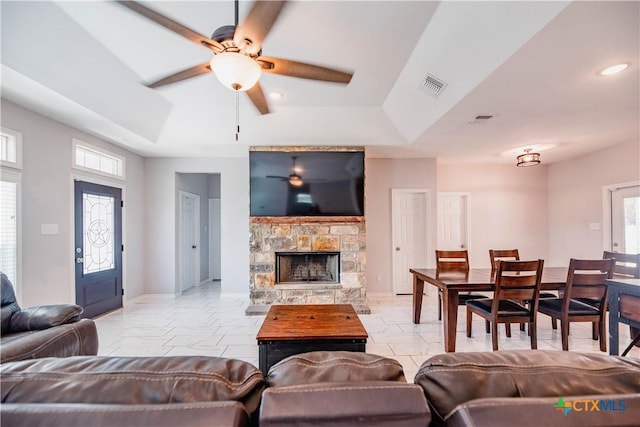 living room featuring marble finish floor, visible vents, a raised ceiling, and a stone fireplace