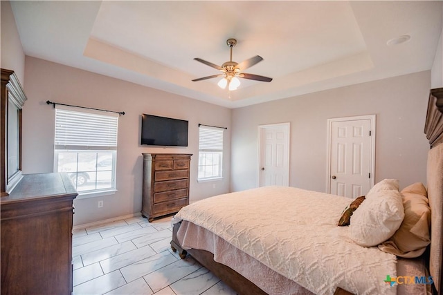 bedroom featuring marble finish floor, ceiling fan, a tray ceiling, and baseboards