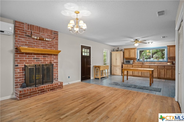 interior space featuring an AC wall unit, wood-type flooring, a fireplace, a textured ceiling, and ceiling fan with notable chandelier