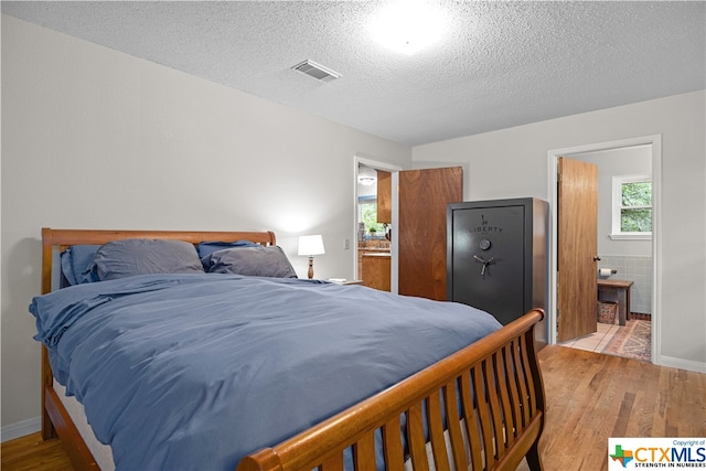 bedroom featuring connected bathroom, a textured ceiling, and light hardwood / wood-style flooring