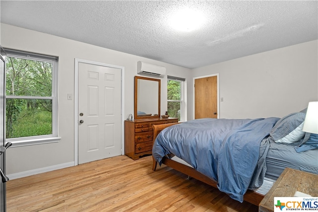 bedroom featuring a wall mounted AC, a textured ceiling, and light hardwood / wood-style floors