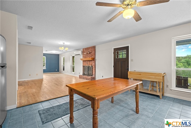 living room featuring a wall mounted AC, light wood-type flooring, a textured ceiling, a brick fireplace, and ceiling fan with notable chandelier