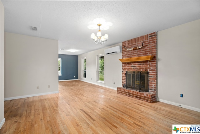 unfurnished living room featuring a brick fireplace, hardwood / wood-style flooring, a textured ceiling, a chandelier, and an AC wall unit