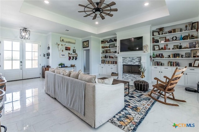 living room featuring marble finish floor, crown molding, a tray ceiling, and built in features