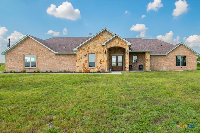 view of front of property featuring a shingled roof, brick siding, stone siding, french doors, and a front lawn