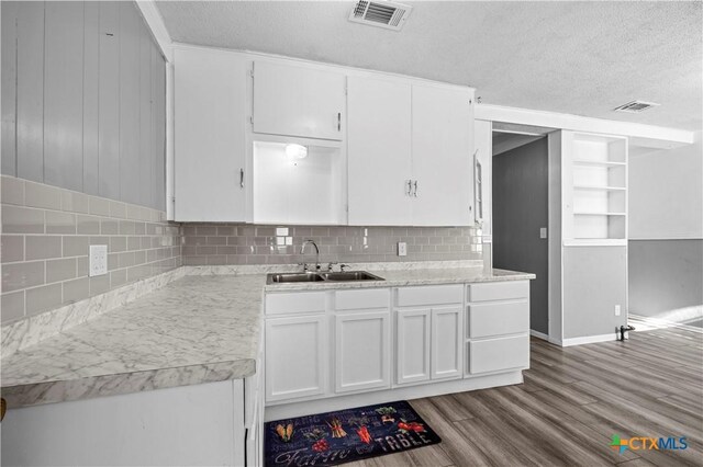 kitchen featuring sink, built in features, a textured ceiling, light wood-type flooring, and white cabinetry