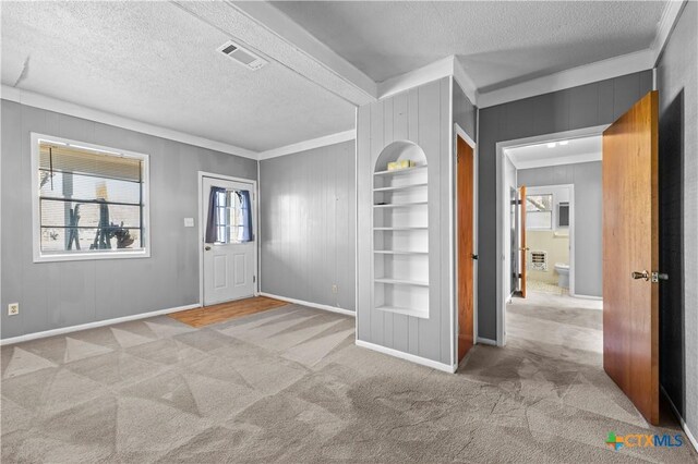 carpeted foyer entrance with wood walls, a textured ceiling, and ornamental molding