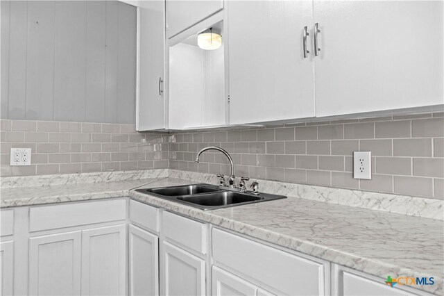 kitchen featuring decorative backsplash, light stone counters, white cabinetry, and sink