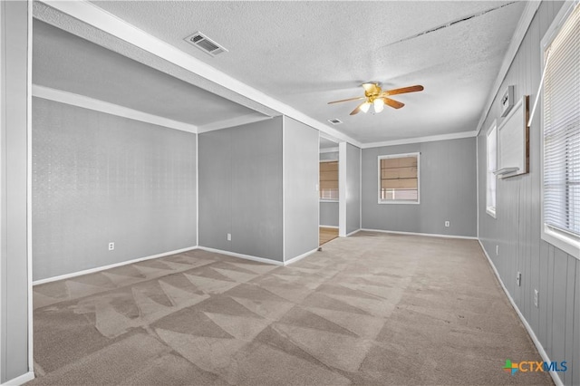 carpeted spare room featuring a healthy amount of sunlight, a textured ceiling, ceiling fan, and crown molding