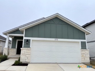 view of front facade with stone siding, a garage, driveway, and board and batten siding