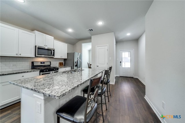 kitchen featuring stainless steel appliances, a sink, visible vents, decorative backsplash, and dark wood-style floors